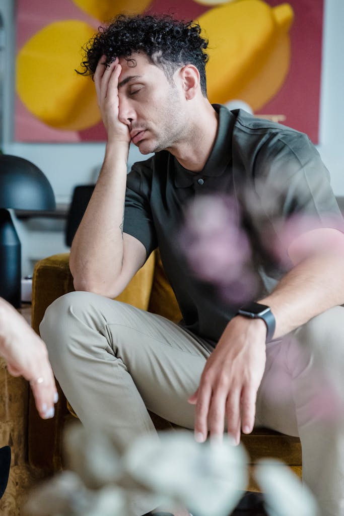 A man sits with his hand on his face, expressing stress during a psychotherapy session.