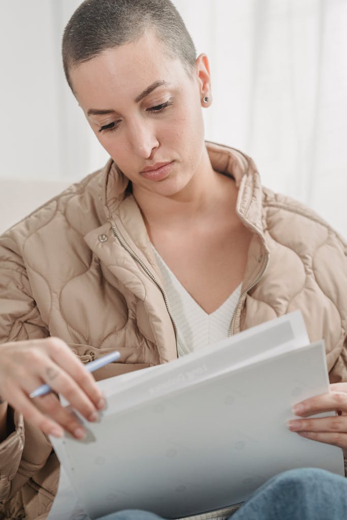 Woman with short hair reading documents indoors, dressed in a quilted jacket with a thoughtful expression.